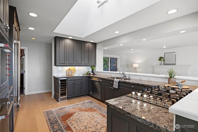 kitchen with appliances with stainless steel finishes, sink, dark stone countertops, backsplash, and light hardwood / wood-style floors