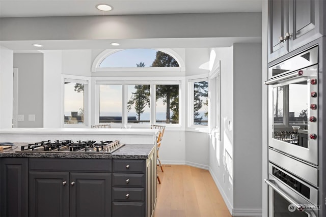 kitchen featuring stainless steel gas cooktop, light hardwood / wood-style floors, and dark stone counters