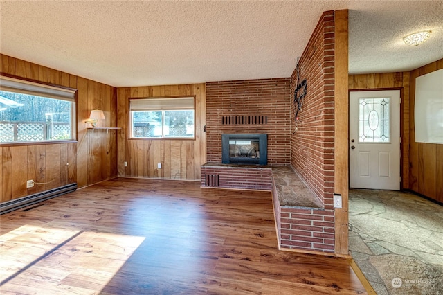 unfurnished living room featuring wooden walls, a fireplace, hardwood / wood-style flooring, a baseboard heating unit, and a textured ceiling