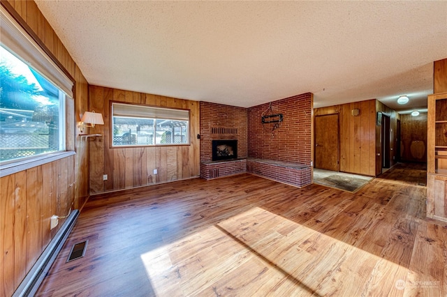 unfurnished living room featuring a brick fireplace, wood-type flooring, a textured ceiling, and a baseboard heating unit