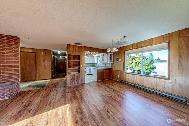 unfurnished living room featuring wooden walls, sink, hardwood / wood-style flooring, baseboard heating, and a textured ceiling