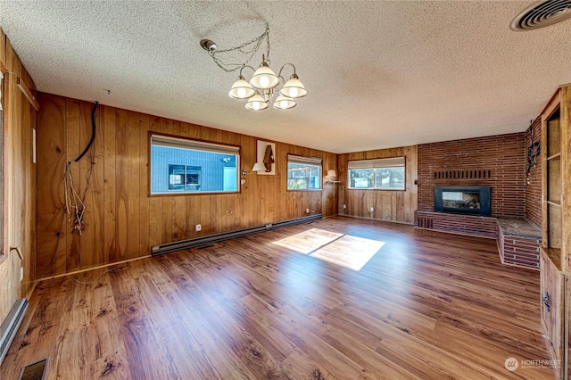 unfurnished living room with an inviting chandelier, wood-type flooring, a textured ceiling, a fireplace, and a baseboard heating unit