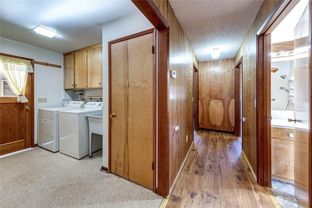 washroom featuring wooden walls, washer and clothes dryer, cabinets, and a textured ceiling