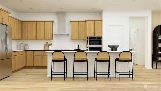 kitchen featuring wall chimney exhaust hood, a breakfast bar, light hardwood / wood-style flooring, appliances with stainless steel finishes, and a kitchen island with sink