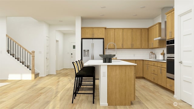 kitchen featuring a breakfast bar, a kitchen island with sink, refrigerator with ice dispenser, light hardwood / wood-style floors, and decorative backsplash