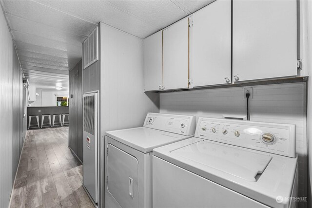 washroom featuring cabinets, washer and clothes dryer, and light hardwood / wood-style flooring