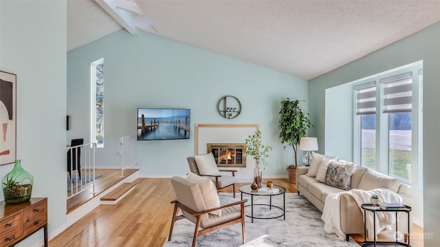 living room with a textured ceiling, light hardwood / wood-style flooring, and vaulted ceiling with beams