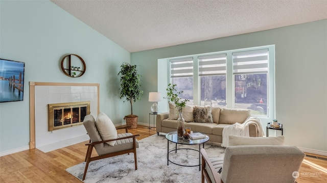 living room with a tile fireplace, vaulted ceiling, a textured ceiling, and light wood-type flooring