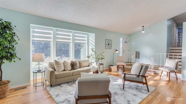 living room with vaulted ceiling, a textured ceiling, and light wood-type flooring