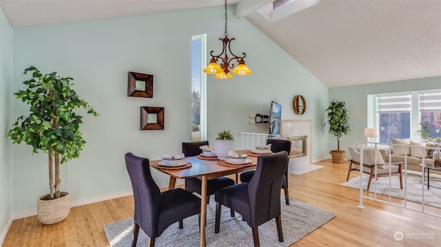 dining room with a tiled fireplace, a notable chandelier, high vaulted ceiling, and light wood-type flooring