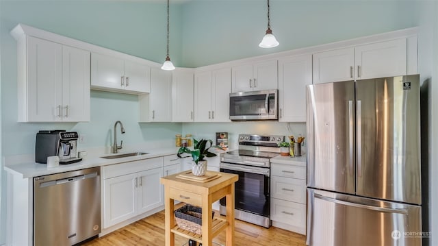 kitchen with sink, light hardwood / wood-style flooring, appliances with stainless steel finishes, white cabinets, and decorative light fixtures