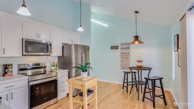 kitchen featuring appliances with stainless steel finishes, white cabinets, pendant lighting, light hardwood / wood-style floors, and a high ceiling