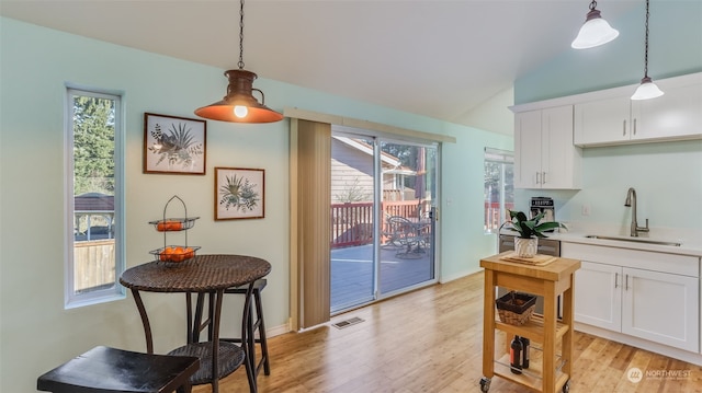 kitchen with lofted ceiling, sink, white cabinets, hanging light fixtures, and light hardwood / wood-style floors