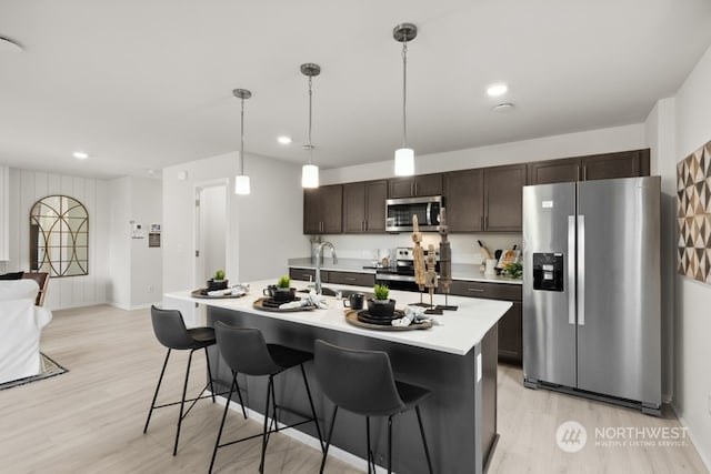 kitchen with light wood finished floors, dark brown cabinetry, light countertops, appliances with stainless steel finishes, and a kitchen breakfast bar