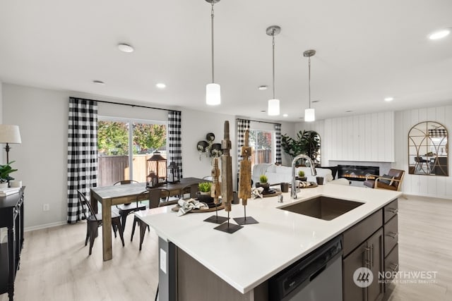 kitchen with a sink, open floor plan, light countertops, a glass covered fireplace, and stainless steel dishwasher