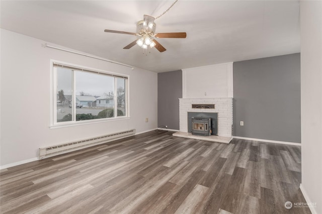 unfurnished living room with a baseboard radiator, dark hardwood / wood-style floors, a wood stove, and ceiling fan