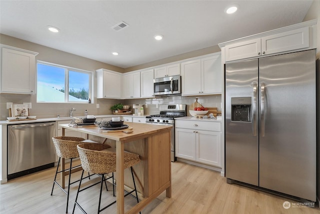 kitchen with stainless steel appliances, white cabinetry, and light hardwood / wood-style floors