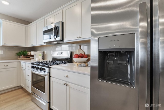 kitchen with tasteful backsplash, white cabinetry, light hardwood / wood-style flooring, and appliances with stainless steel finishes