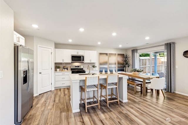 kitchen featuring appliances with stainless steel finishes, sink, white cabinets, a kitchen island with sink, and light wood-type flooring