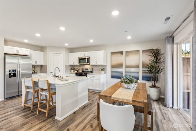 kitchen featuring a breakfast bar, appliances with stainless steel finishes, a kitchen island with sink, white cabinetry, and light hardwood / wood-style floors