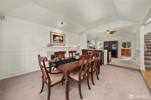 dining area featuring light carpet, stairs, lofted ceiling, and a premium fireplace