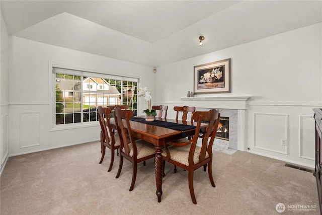 dining area featuring visible vents, light colored carpet, a premium fireplace, and a decorative wall