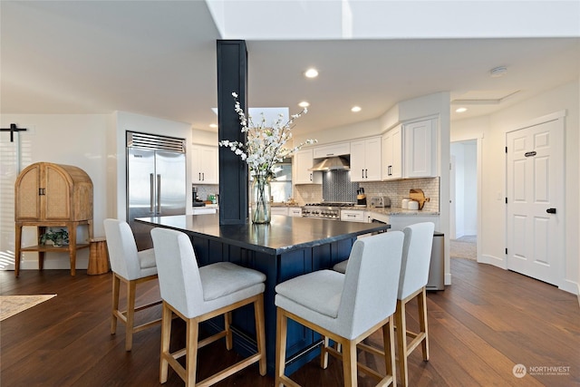 kitchen with stove, white cabinets, a kitchen island, dark hardwood / wood-style flooring, and built in fridge