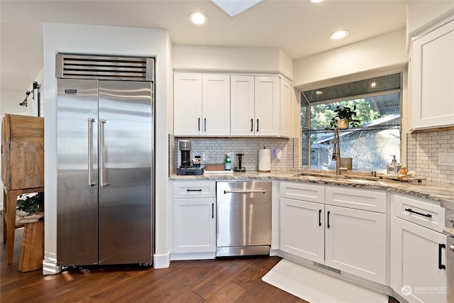 kitchen with built in fridge, white cabinetry, backsplash, light stone countertops, and dark wood-type flooring