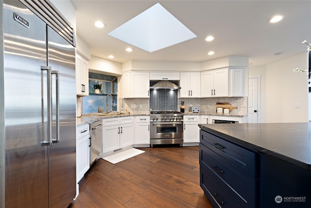 kitchen with high end appliances, wall chimney range hood, white cabinetry, and sink