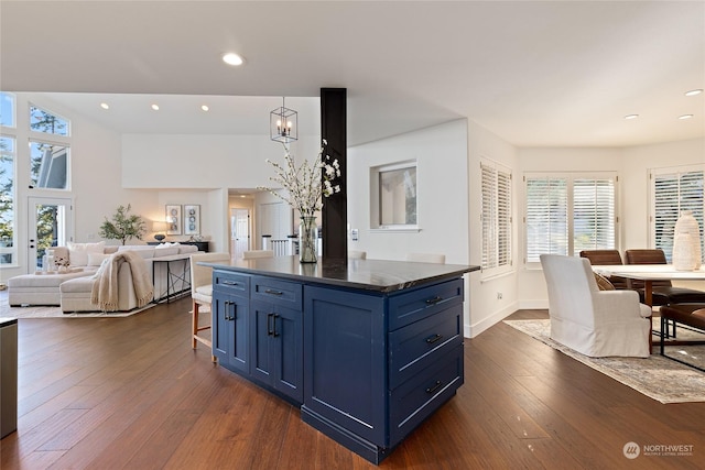 kitchen with dark wood-type flooring, blue cabinetry, an inviting chandelier, a kitchen island, and a kitchen bar