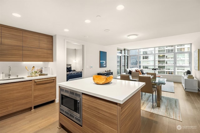 kitchen featuring stainless steel microwave, sink, a kitchen island, and light wood-type flooring