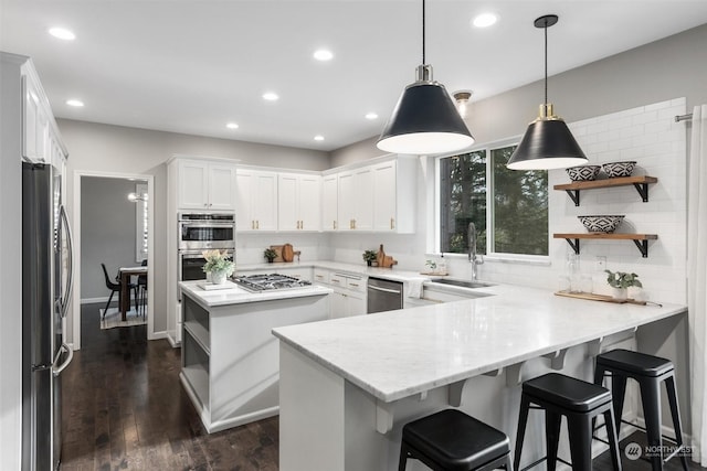 kitchen with appliances with stainless steel finishes, decorative light fixtures, sink, white cabinets, and kitchen peninsula