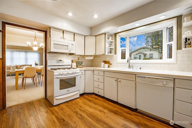 kitchen with sink, white appliances, light hardwood / wood-style floors, white cabinets, and decorative light fixtures