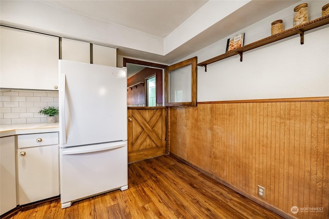 kitchen featuring white cabinetry, hardwood / wood-style floors, white fridge, decorative backsplash, and wood walls