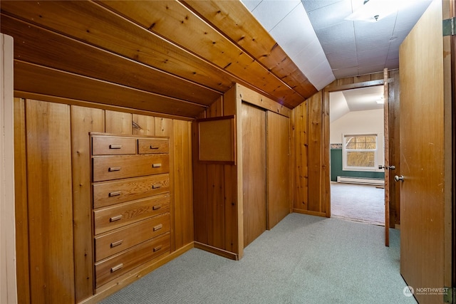 hall with vaulted ceiling, light colored carpet, wood walls, and baseboard heating