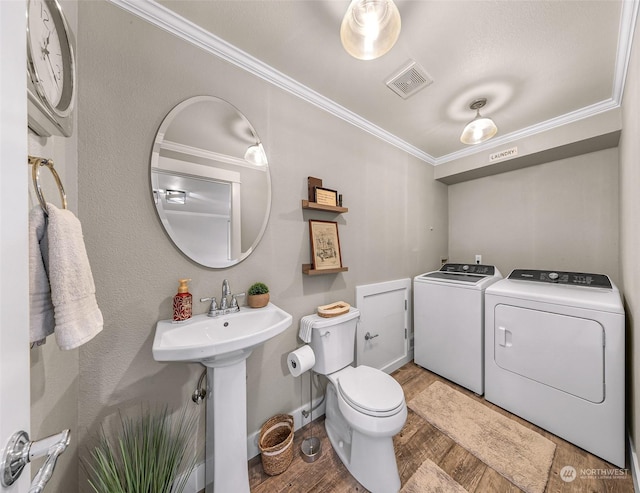 bathroom with toilet, sink, crown molding, separate washer and dryer, and hardwood / wood-style floors