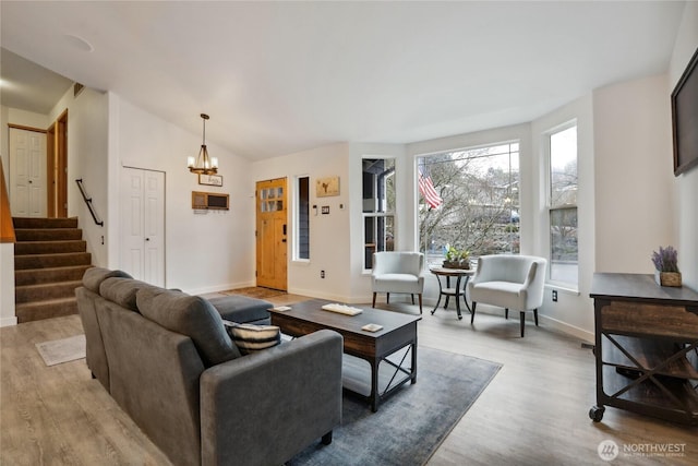 living area with wood finished floors, an inviting chandelier, baseboards, stairs, and vaulted ceiling