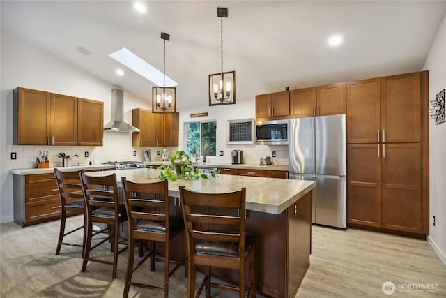 kitchen with a center island, wall chimney range hood, vaulted ceiling with skylight, a notable chandelier, and stainless steel appliances