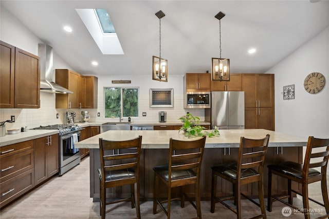 kitchen featuring light countertops, appliances with stainless steel finishes, lofted ceiling with skylight, wall chimney range hood, and tasteful backsplash