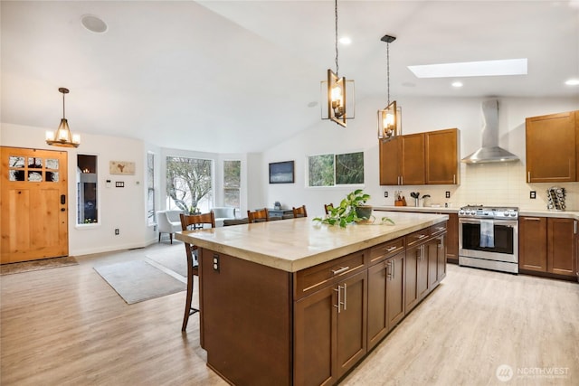 kitchen with light wood finished floors, stainless steel range with gas cooktop, wall chimney range hood, a chandelier, and vaulted ceiling with skylight