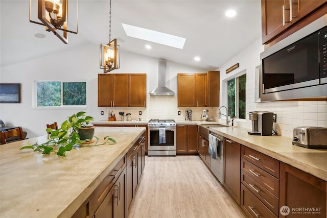 kitchen with a sink, appliances with stainless steel finishes, wall chimney exhaust hood, and light countertops