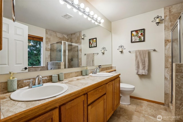 bathroom featuring a shower stall, toilet, double vanity, and a sink