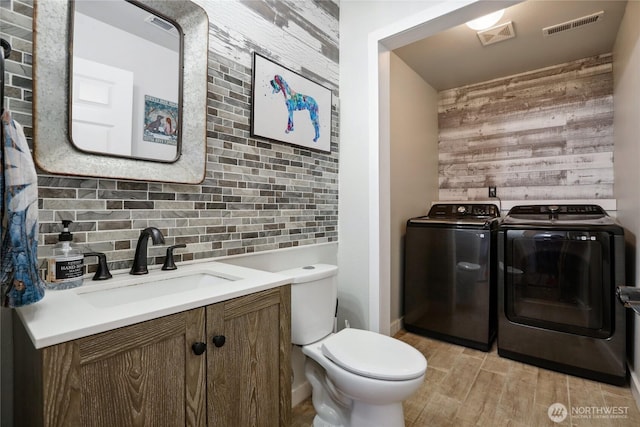 half bathroom with vanity, wood finished floors, visible vents, washer and dryer, and toilet