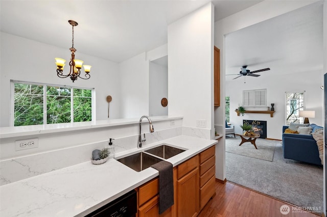 kitchen with decorative light fixtures, brown cabinetry, open floor plan, a sink, and a lit fireplace