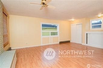 unfurnished living room with ceiling fan, a baseboard radiator, a healthy amount of sunlight, and hardwood / wood-style floors