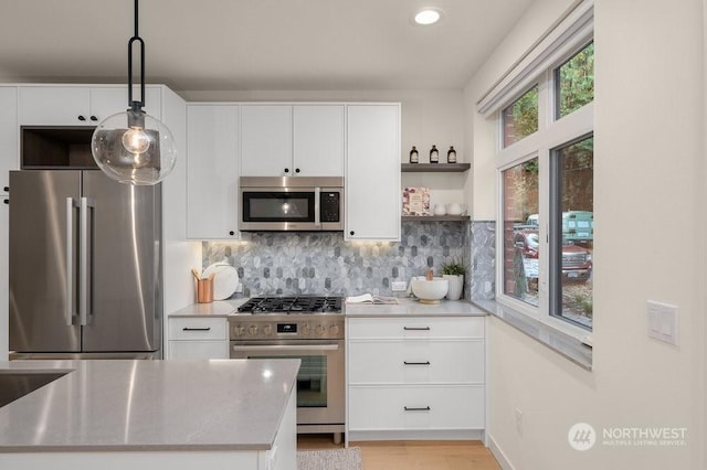 kitchen with pendant lighting, appliances with stainless steel finishes, white cabinetry, tasteful backsplash, and light hardwood / wood-style floors