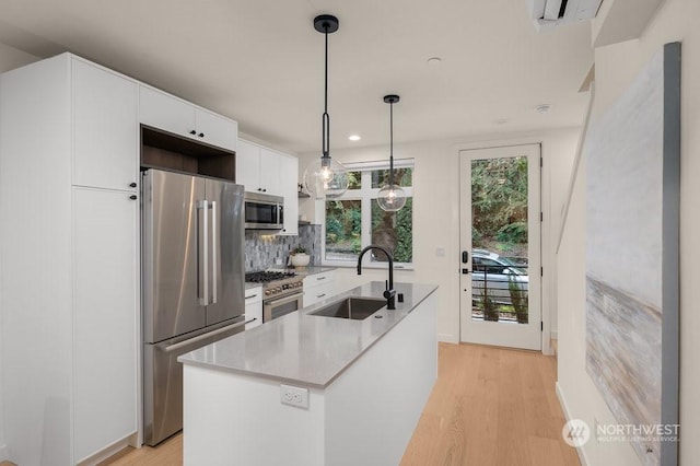 kitchen with pendant lighting, high quality appliances, white cabinetry, sink, and a center island with sink