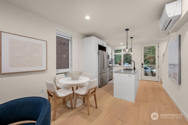 kitchen featuring white cabinetry, a wall mounted air conditioner, decorative light fixtures, appliances with stainless steel finishes, and light hardwood / wood-style floors