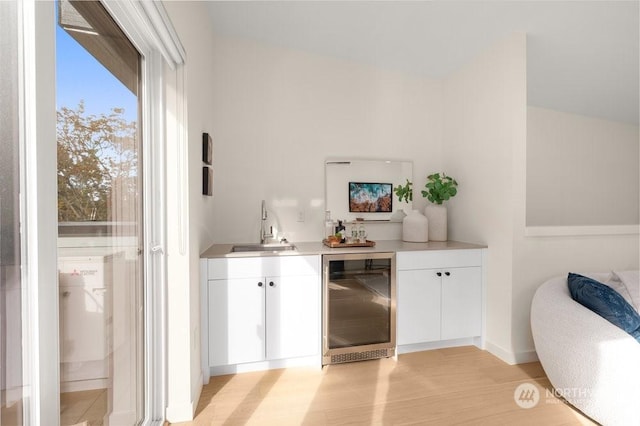 bar with light wood-type flooring, beverage cooler, sink, and white cabinets