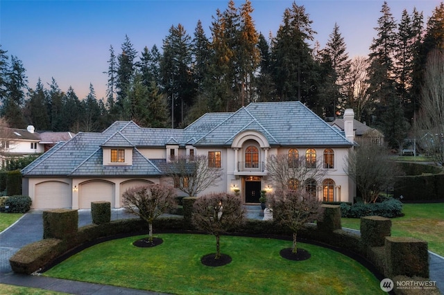 french country home with an attached garage, a front yard, and stucco siding